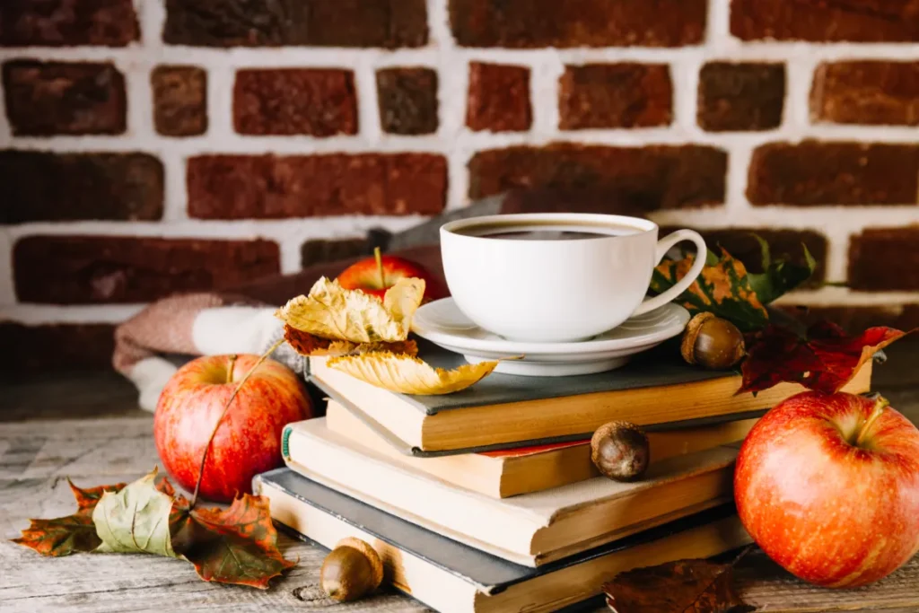 Купчина стари книги с чаша кафе, ябълки и есенни листа на дървена маса
