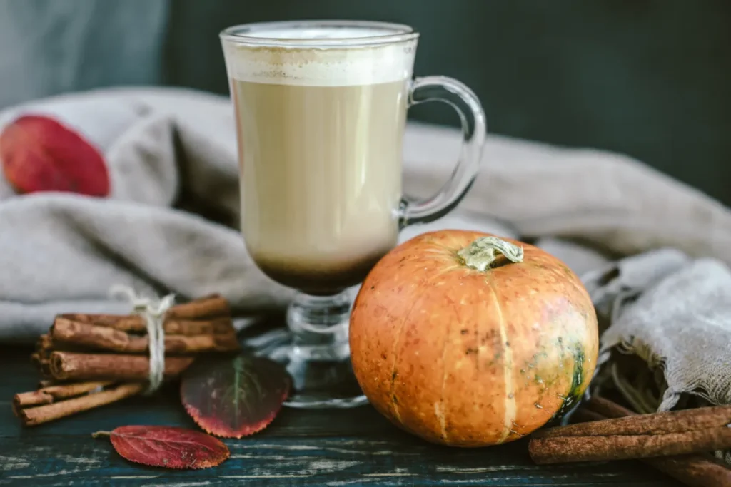 Домашно pumpkin spice лате в стъклена чаша с тиква и канелени пръчки на дървена маса